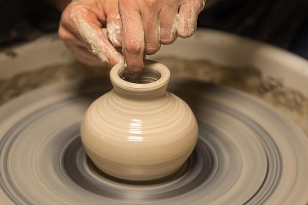 A close up of a small vase being wheel thrown with two hands on a potters wheel.