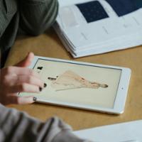 Two pairs of hands use an ipad to study a dress design