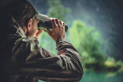 Man in jacket and hat looking through binoculars in forest