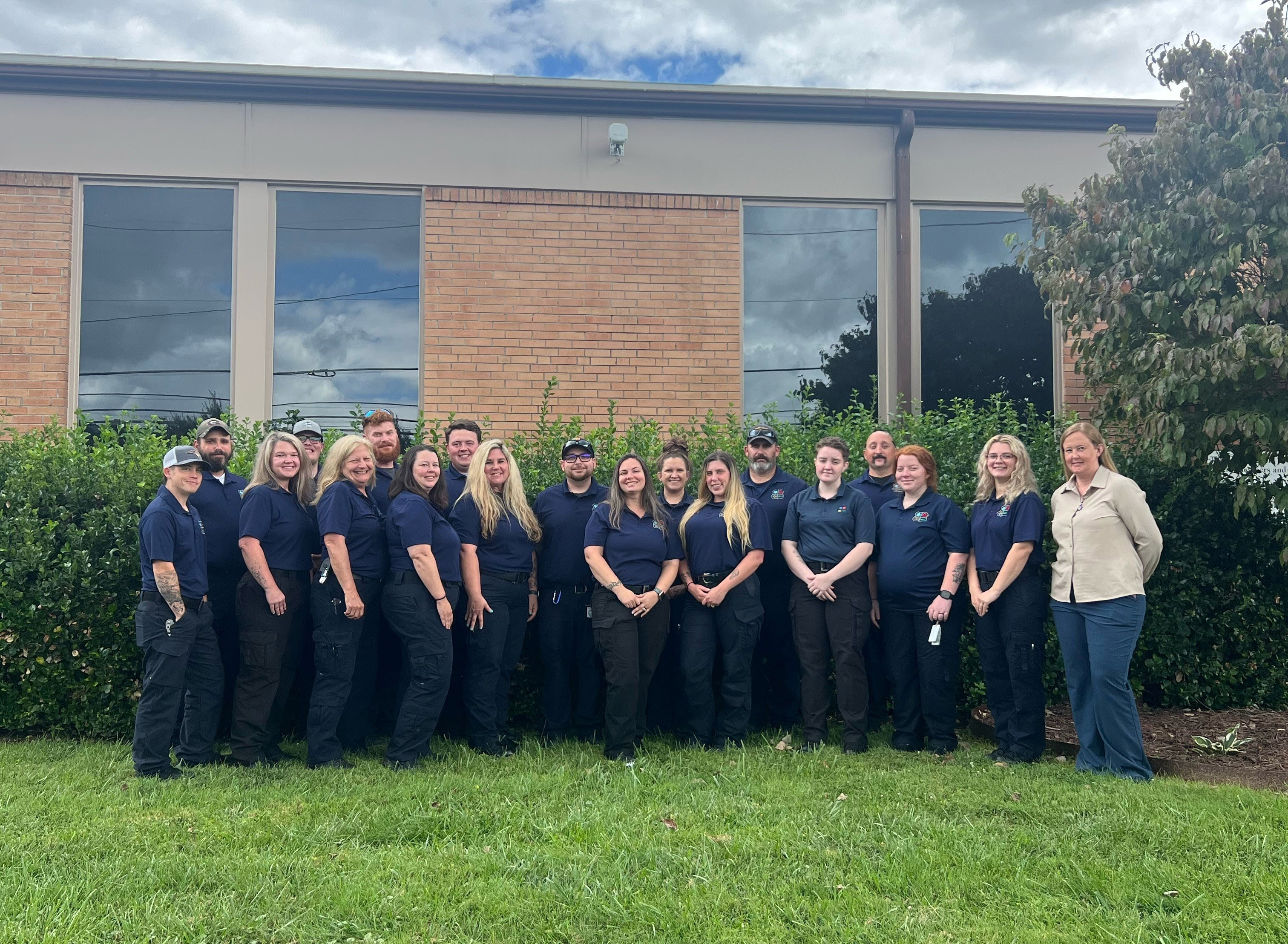 18 paramedic graduates with their instructor outside of building on campus